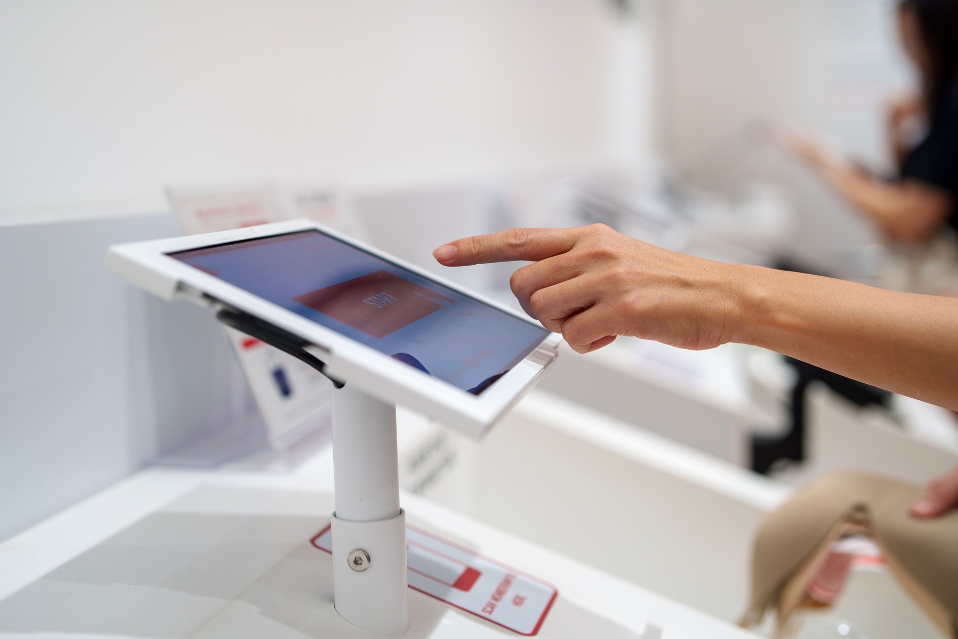 Side view of a woman using touch screen display to start an order or payment for a product or service at a kiosk machine in a shopping mall