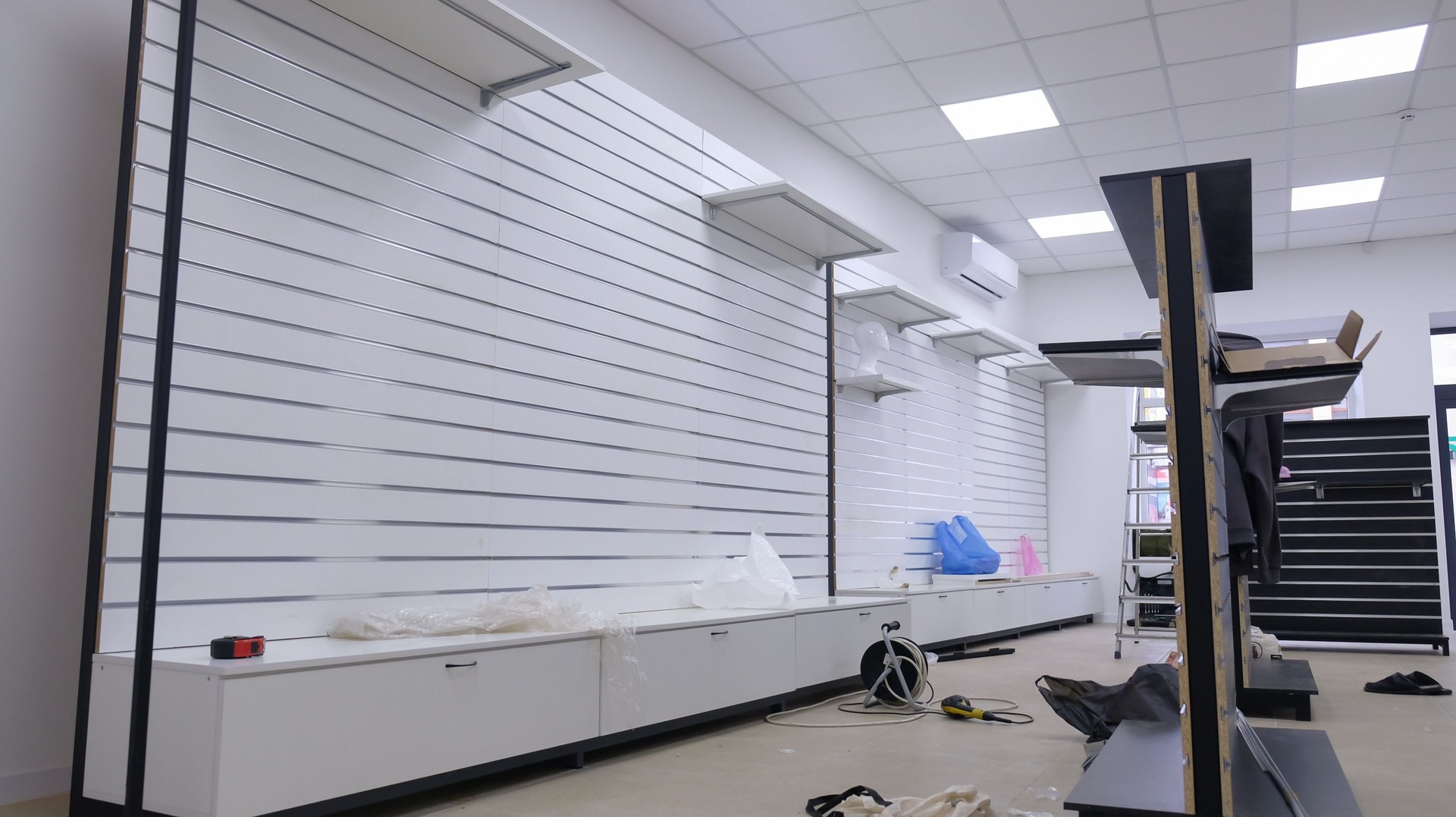 The store premises at the stage of equipment installation and interior arrangement. White panels with metal inserts for placing goods are fixed on the wall.
